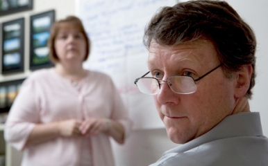 Two staff look at the camera with a whiteboard behind them