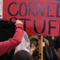 Student holds up a shirt before a sign reading "Cornell Stuff"