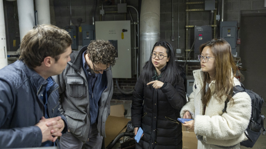 Staff and students converse inside a mechanical room filled with industrial equipment.