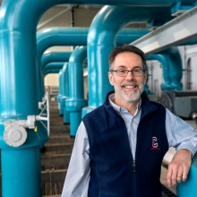 Lanny Joyce, former director of utilities and energy management and the LSC project manager, standing in front of LSC pipes. 