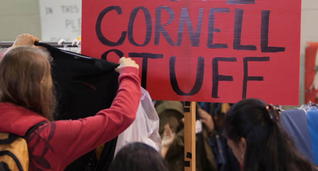 Student holds up a shirt before a sign reading "Cornell Stuff"